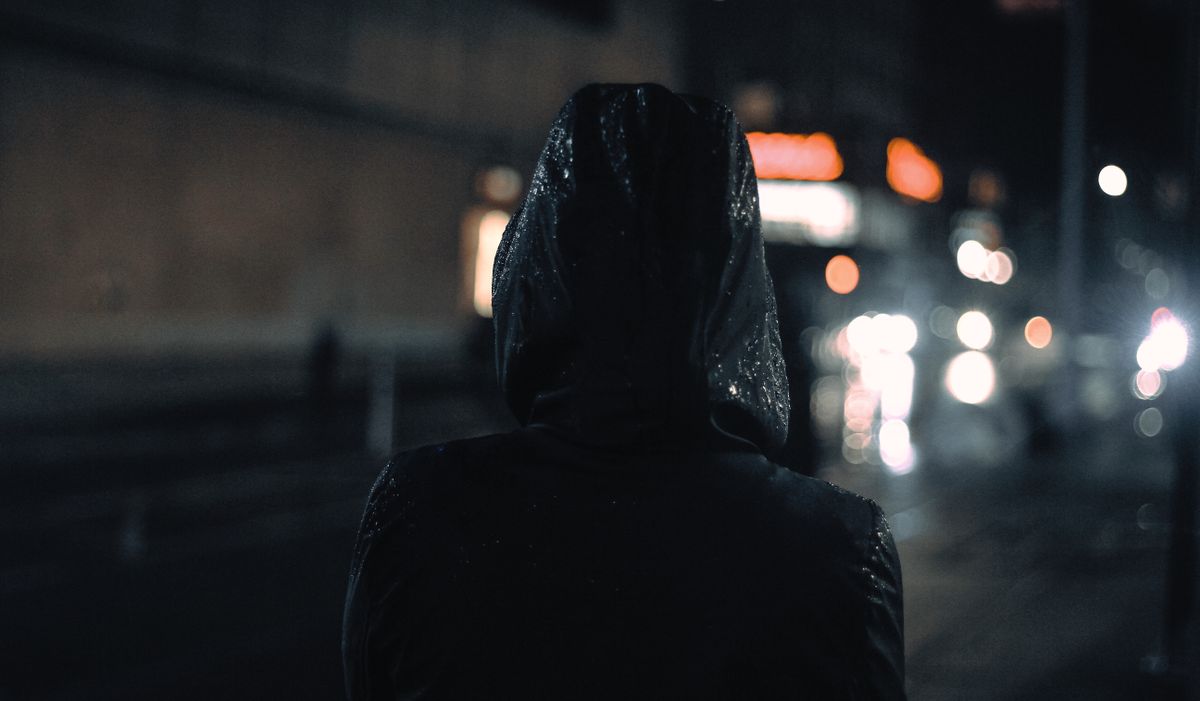 Persona encapuchada de espaldas en una calle de noche, denunciar sin datos del autor