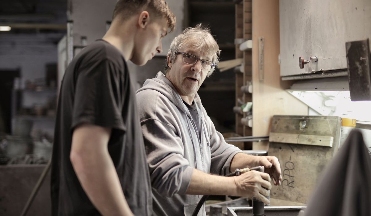 Instructor mostrando a un alumno trabajador cómo manejar una herramienta en un taller de empleo