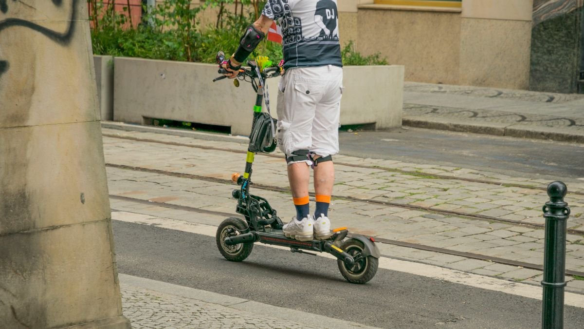 Hombre circulando de pie en un patinete eléctrico por una calle de ciudad