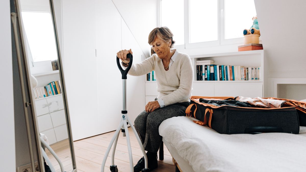 mujer mayor con andador sentada junto a una maleta preparando un viaje, pension no contributiva y dias fuera de españa