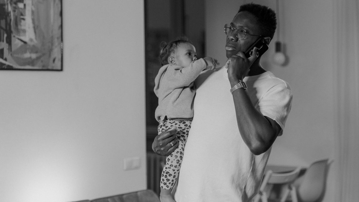 Un padre con su bebe en brazos habla por telefono mientras concilia el cuidado y el trabajo