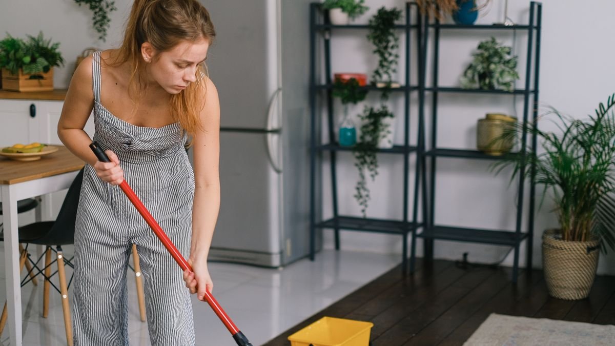 Trabajadora de limpieza inclinada fregando el suelo, con esfuerzo en la espalda