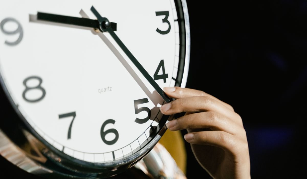 Una mano mueve las agujas de un reloj de pared para el cambio de hora