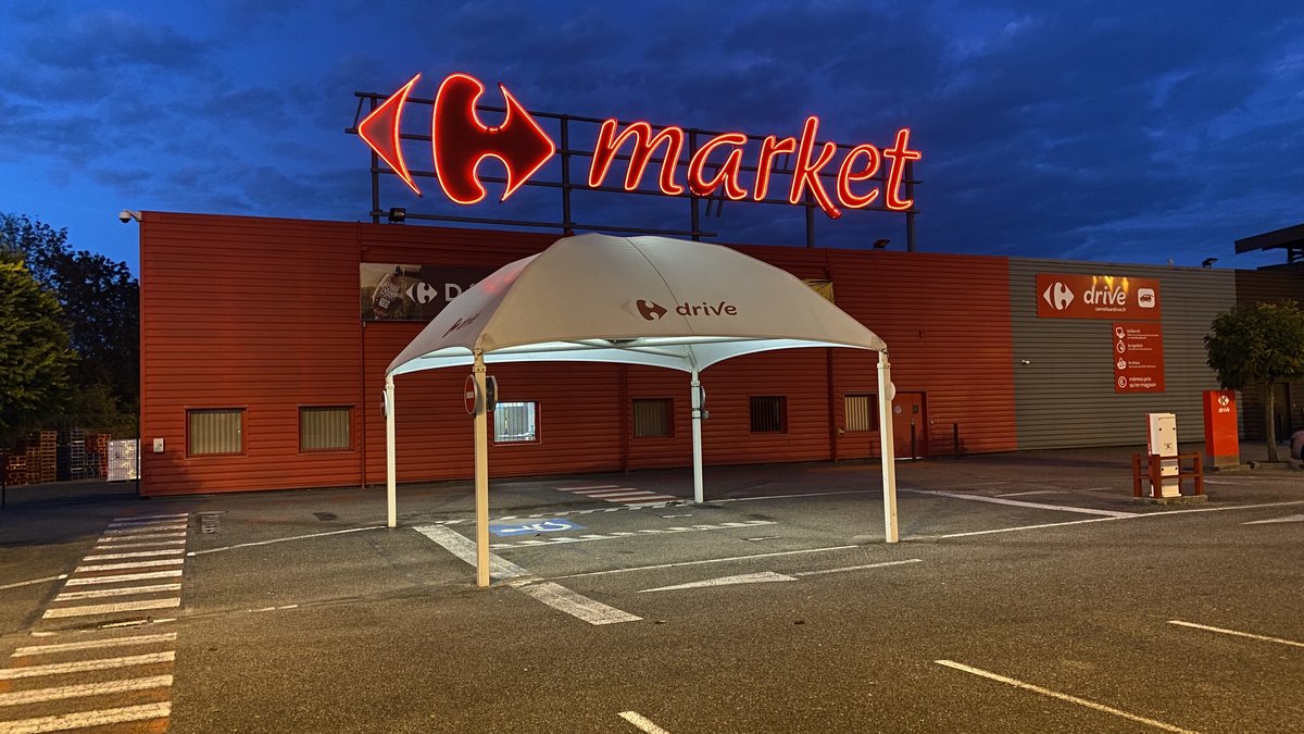 Fachada de un supermercado Carrefour Market con el rótulo iluminado al anochecer, empresa condenada por el despido improcedente de una dependienta por un cupón de descuento