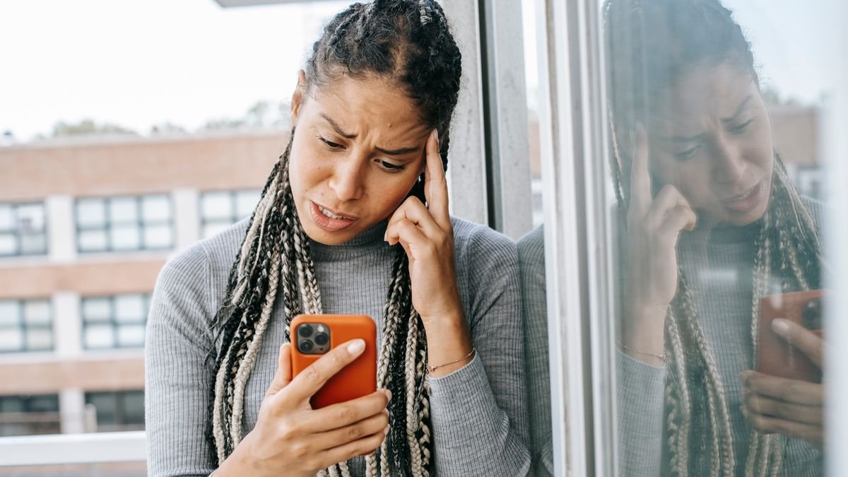 Mujer joven angustiada mirando el móvil, víctima de desnudos falsos creados con IA