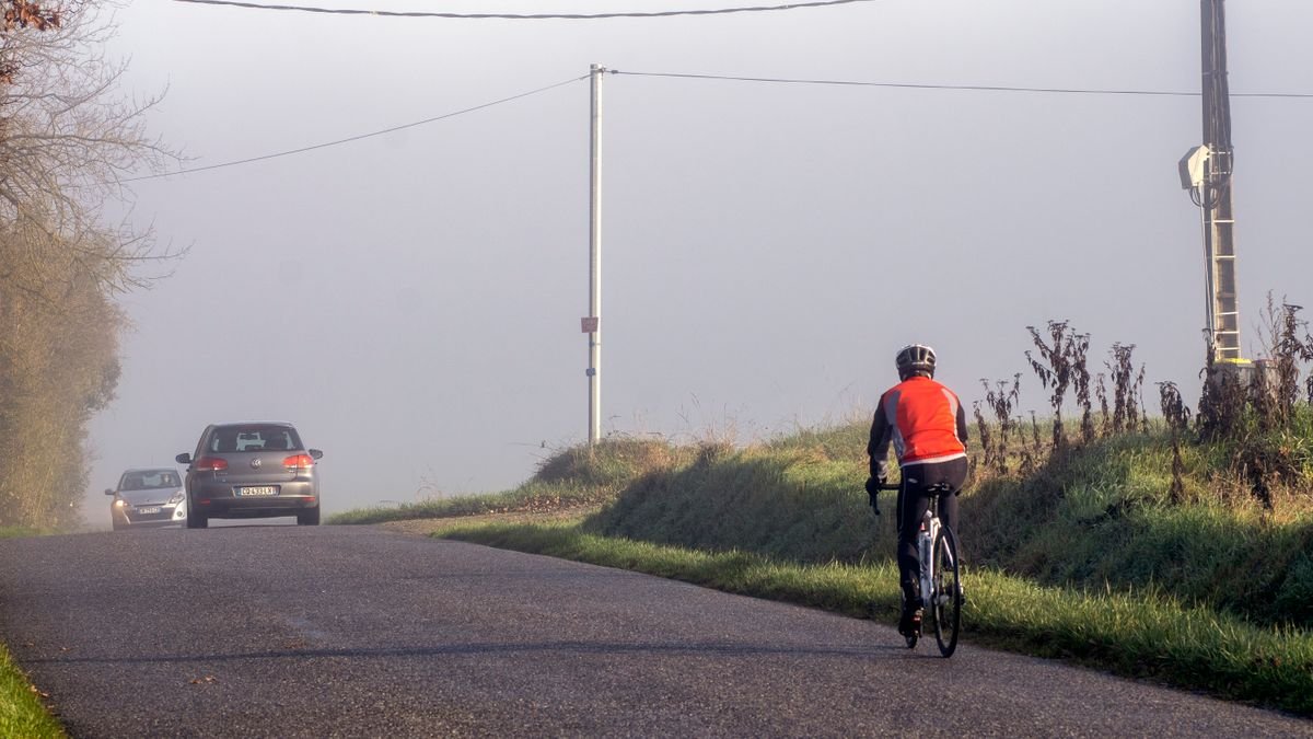 Ciclista circulando por el arcén de una carretera interurbana con un coche aproximándose por detrás