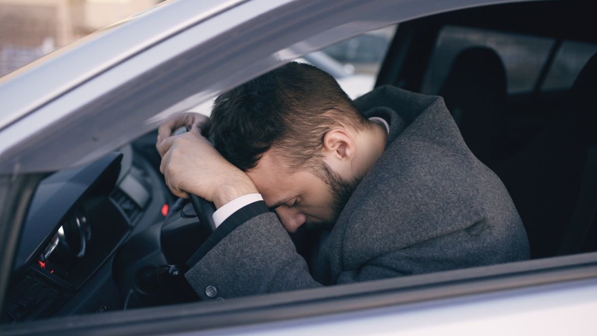 Hombre abatido con la cabeza apoyada en el volante del coche, agotado por la depresión